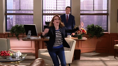 woman running and celebrating in an office with a man behind her