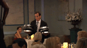 a waiter in a suit dancing and holding serving trays