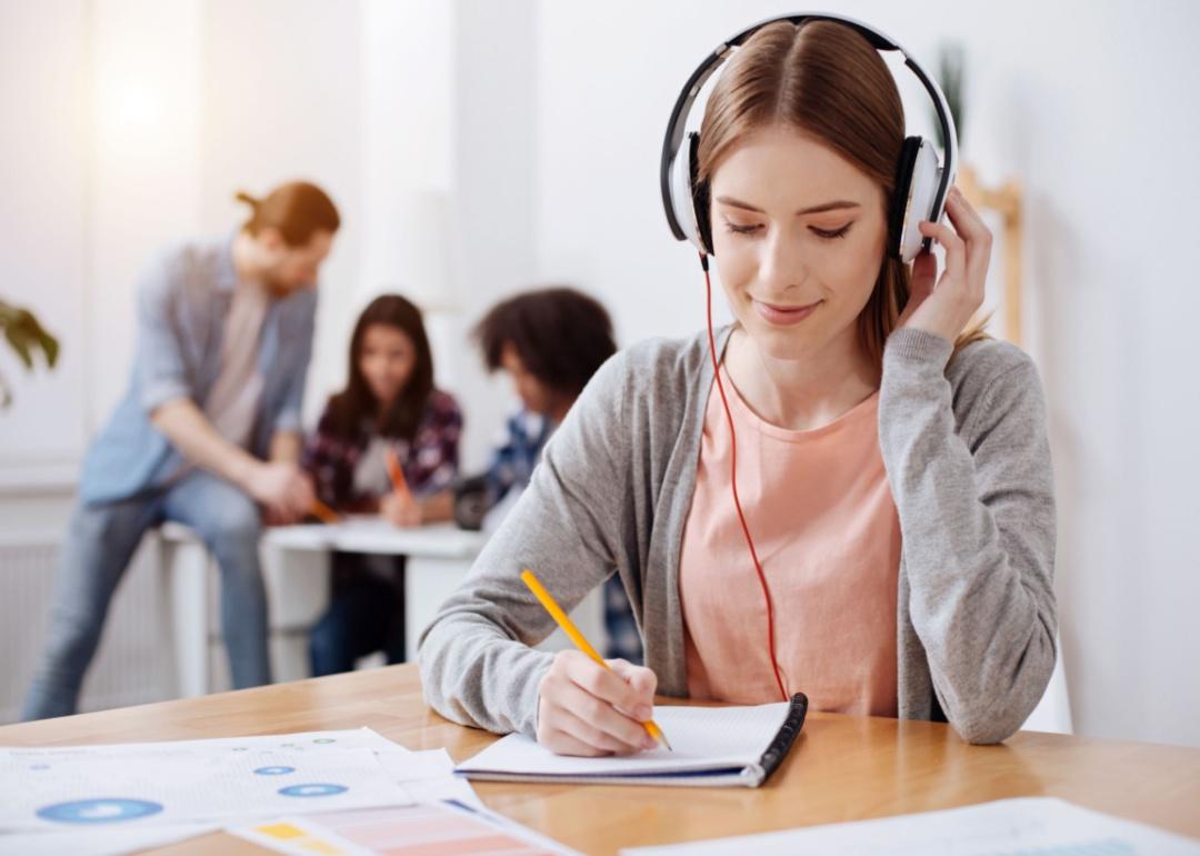 A woman with headphones on and writing on a notebook