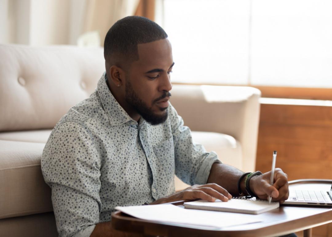 A person sitting in front of a couch and writing in a notebook 