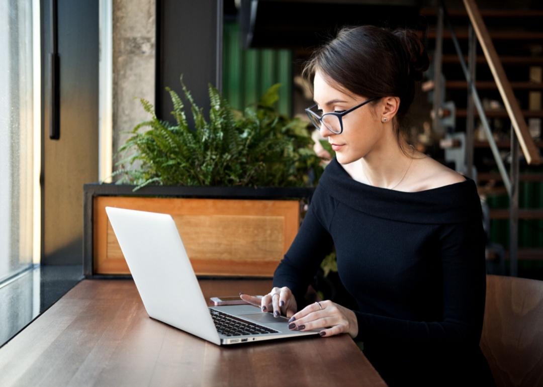 Seorang wanita berkacamata sedang bekerja di depan laptop