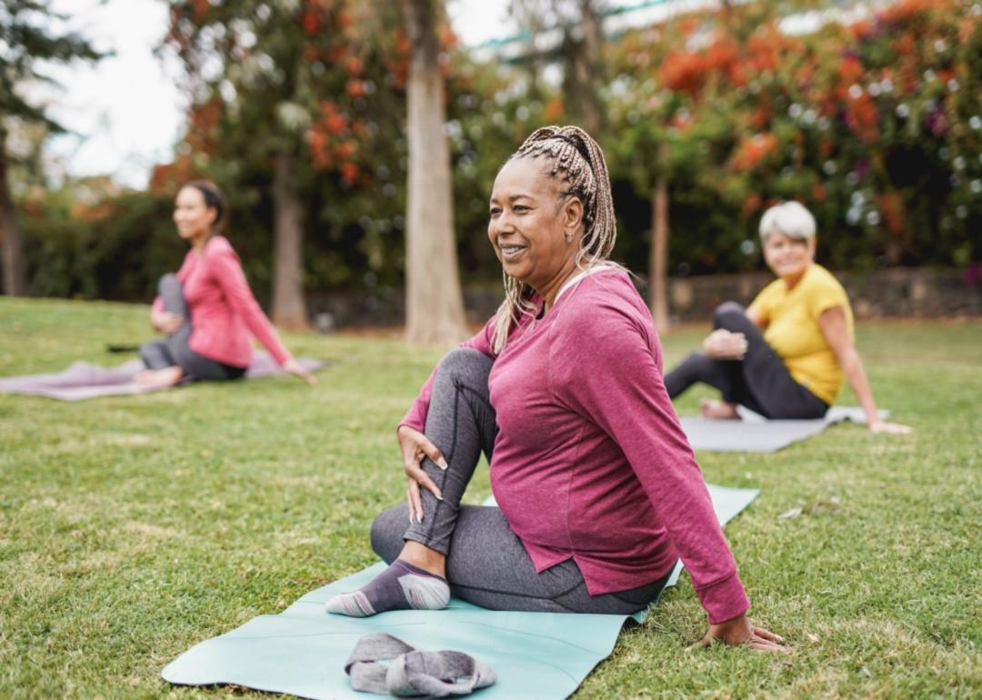 Three women stretching and exercises on their yoga mats in the grass