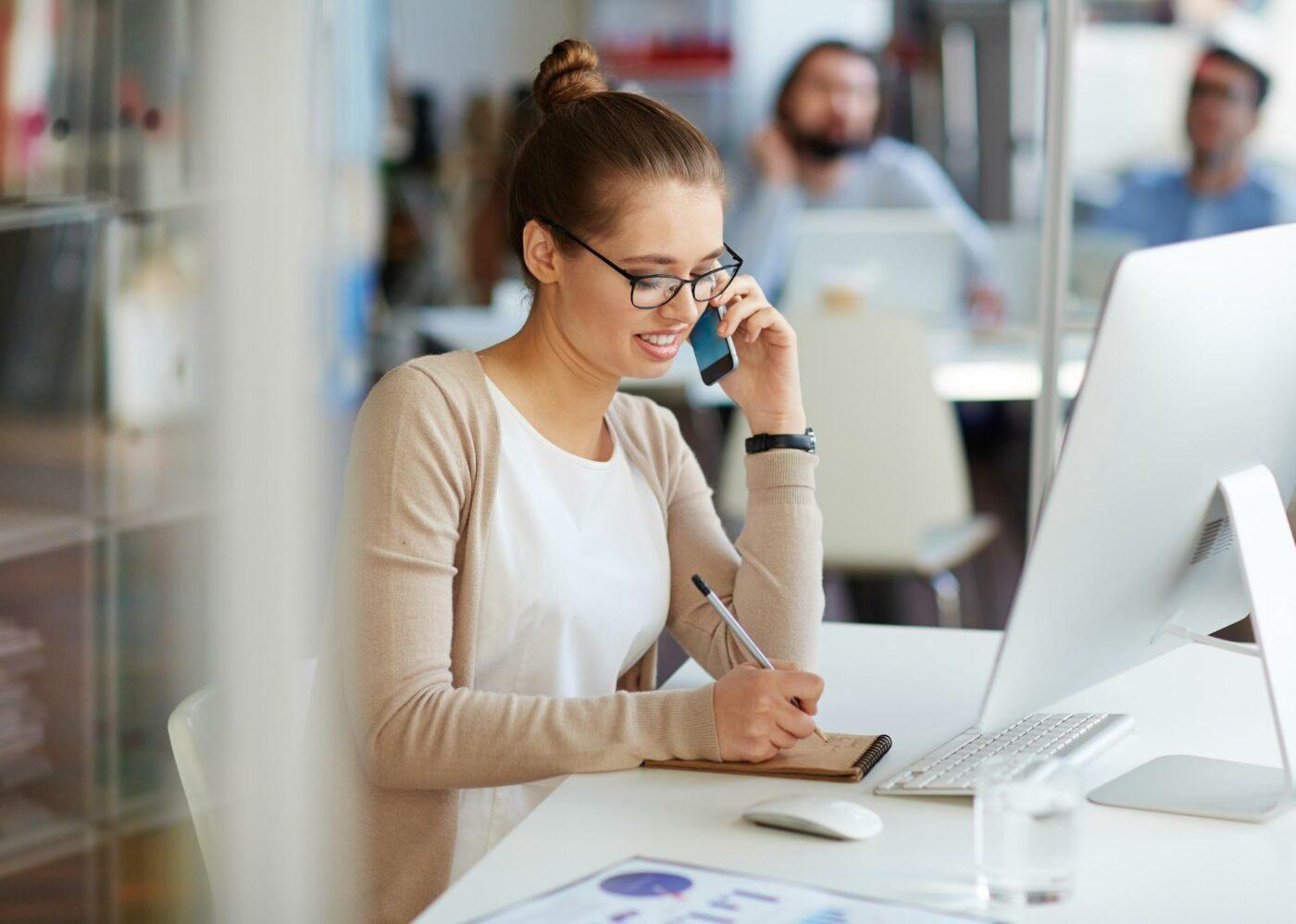 Una donna che scrive note su un foglio di carta mentre parla al telefono